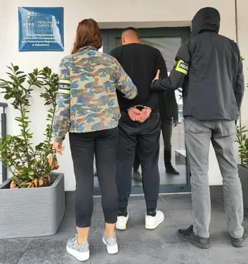 Funkcjonariusze policji prowadzą zatrzymanego w kajdankach do siedziby Prokuratury Europejskiej EPPO w Katowicach.