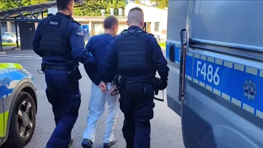 Funkcjonariusze policji prowadzą zatrzymanego mężczyznę w kajdankach do radiowozu oznaczonego F486.