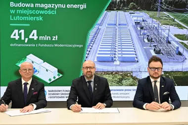 Trzej mężczyźni w garniturach podpisują dokumenty przy stole, w tle baner informujący o budowie magazynu energii w Lutomiersku z dofinansowaniem 41,4 mln zł z F